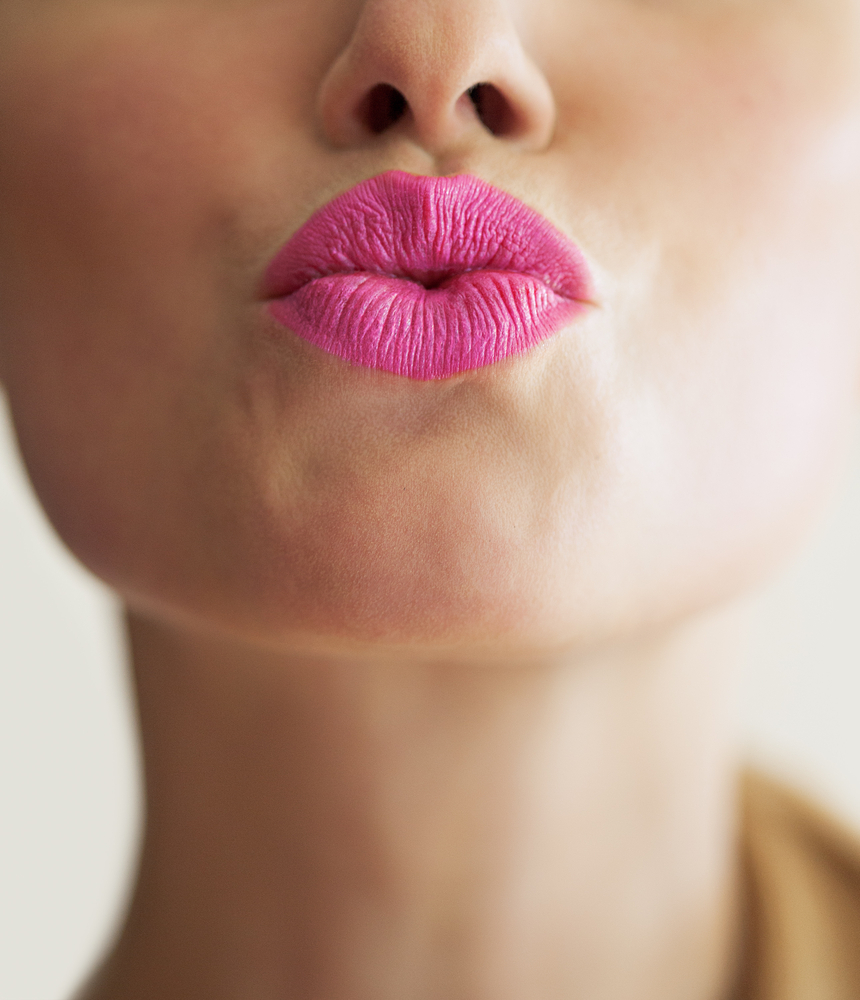 Mund mit pinkem Lippenstift macht Kussmund in Kamera