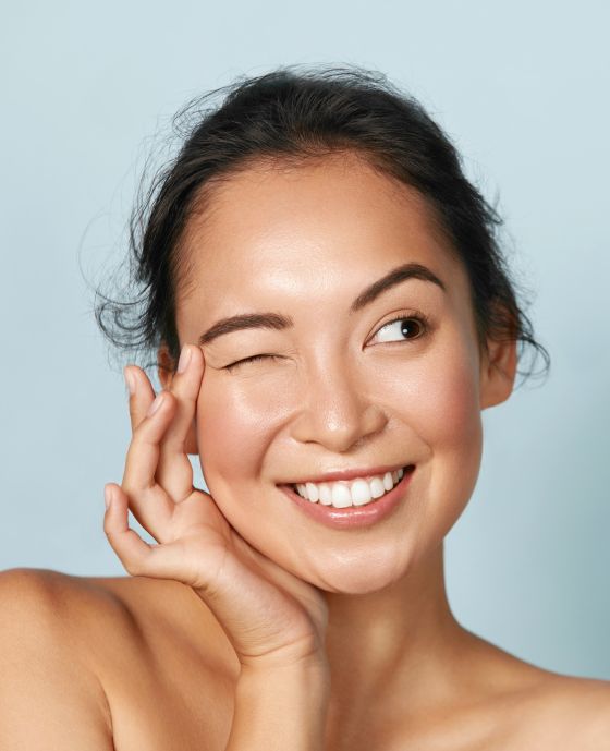 Junge Frau zieht Krähenfüße am Auge lächelnd zusammen