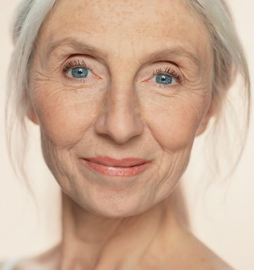 Frau mittleren Alters mit leichten hängenden Unterlidern lächelt in Kamera