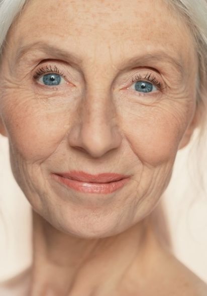 Frau mittleren Alters mit leichten hängenden Unterlidern lächelt in Kamera