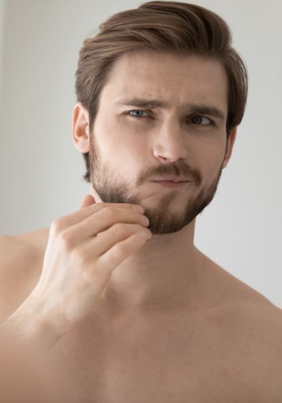 Spiegelbild eines jungen brünetten Mannes der seine Gesichtshaut kritisch betrachtet