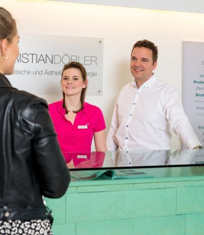 Dr. Döbler und Mitarbeiterin begrüßen Patientin an der Rezeption